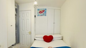 A small, neatly arranged bedroom with a bed, a red heart-shaped pillow, a blue blanket, and a painting of a flower on the wall. - Brighton charm – Near Beach, City Centre & Station (Brighton and Hove)