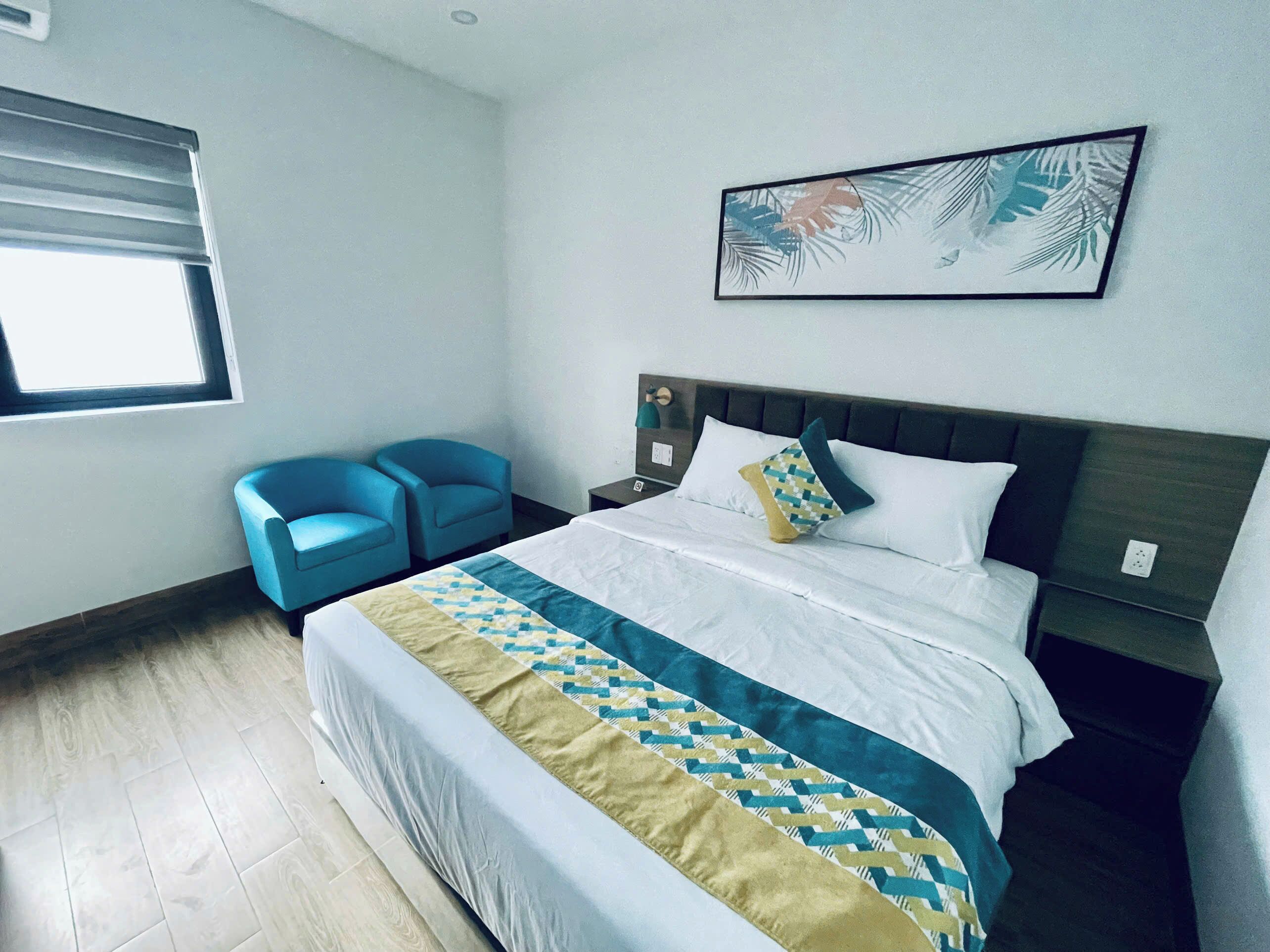 Een hotelkamer met een groot bed, twee blauwe stoelen, een nachtkastje en een schilderij aan de muur.