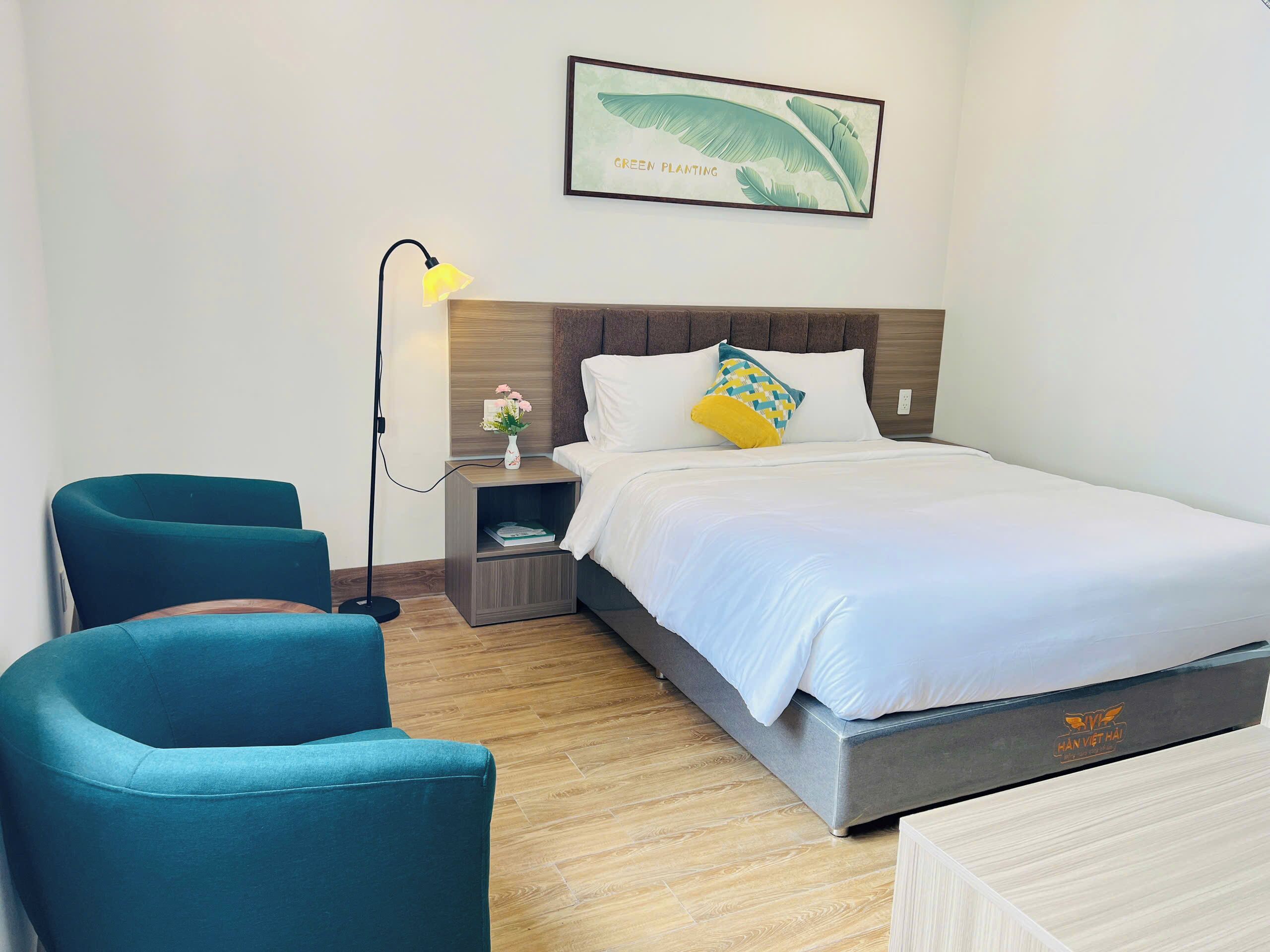 Une chambre d’hôtel avec un lit, deux chaises, une table de chevet avec une lampe et un tableau encadré au mur.