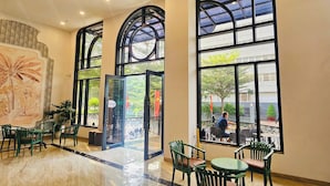A spacious indoor area with large windows, green chairs, and a tiled floor.