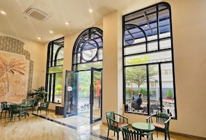Un espacio interior amplio con ventanas grandes, sillas verdes y piso de baldosas.
