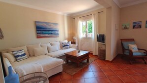 A living room with a sofa, a wooden coffee table, a wicker chair, and a TV. - Ferienhaus 4 Personen in Son Moja Santanyí, 900 m von der Cala Santanyí (Santanyi)