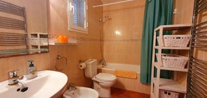 Une salle de bain équipée d’un lavabo, de toilettes, d’une baignoire et d’étagères où sont rangés les produits de toilette.