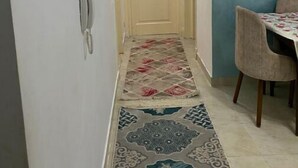 A narrow hallway with a patterned rug, a door at the end, and a dining area with a table and chairs. - Cozy Modern Apartment in El Rehab 2, (Cairo Governorate)