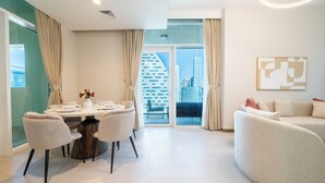 A modern living room with a sofa, a dining table with chairs, and a view of a cityscape through a glass door. - 1BR Home – Luxury & Comfort Combined (Dubai)