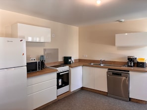 A modern kitchen with white cabinets, a built-in oven, a dishwasher, a stove, and a coffee maker.