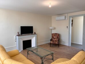 A living room with a fireplace, a television, a patterned armchair, and a glass coffee table.