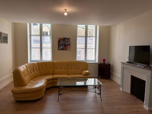 A living room with a leather sofa, a glass coffee table, a television on a stand, and a fireplace.