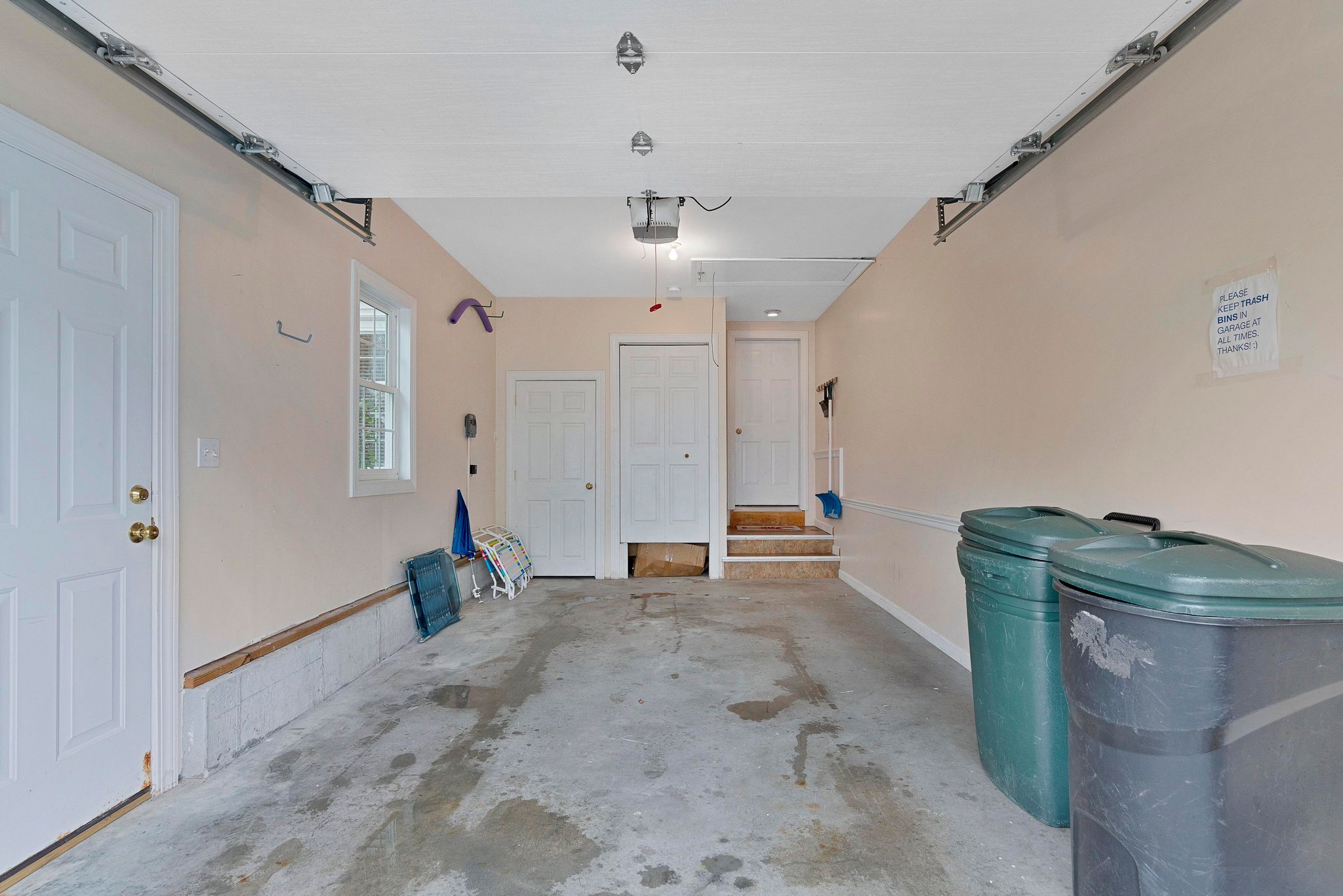 Un couloir avec un sol en béton, des portes blanches et des poubelles.
