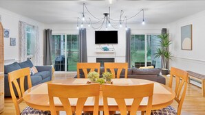 Una sala de estar moderna con una mesa de comedor redonda de madera, dos sofás y un televisor montado en la pared.