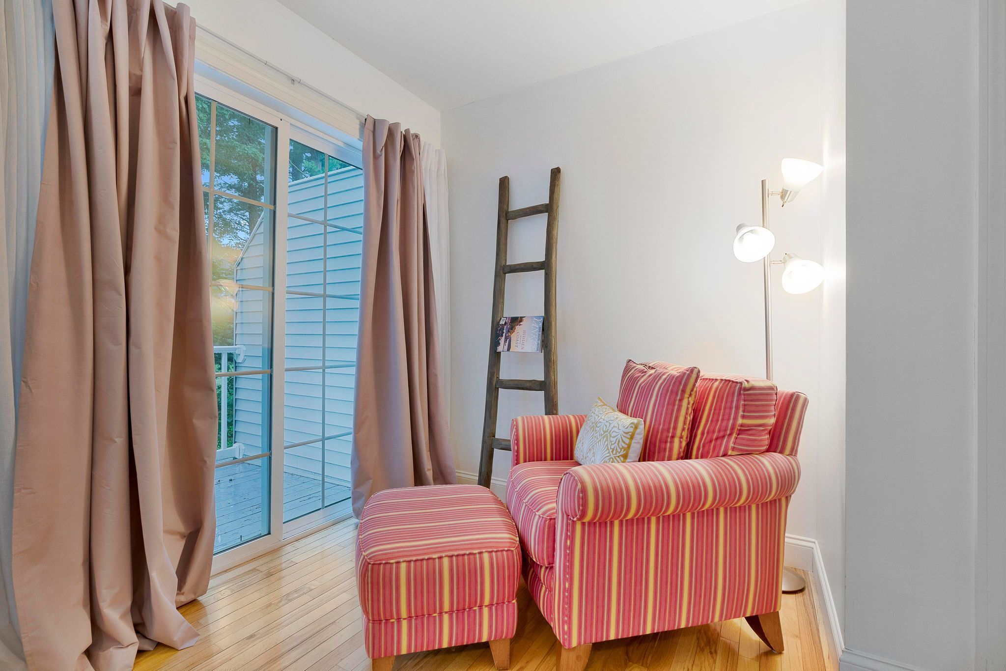 Une pièce avec un canapé à rayures, un pouf, une échelle et un lampadaire.