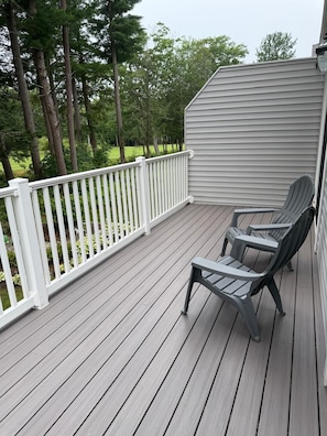 Une terrasse en bois avec une balustrade blanche, deux fauteuils Adirondack et une vue sur un paysage verdoyant.