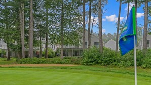 Un campo de golf con una bandera, árboles y casas al fondo.