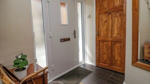 Un couloir avec une porte blanche, une porte en bois, une petite table avec une plante et une chaise.