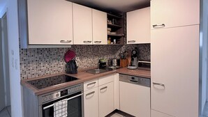 Een moderne keuken met witte kasten, een inbouwoven, een vaatwasser en een betegelde spatwand.