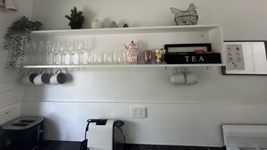Una cocina con estantes blancos que contienen diversos objetos como vasos, una caja de té y utensilios de cocina.