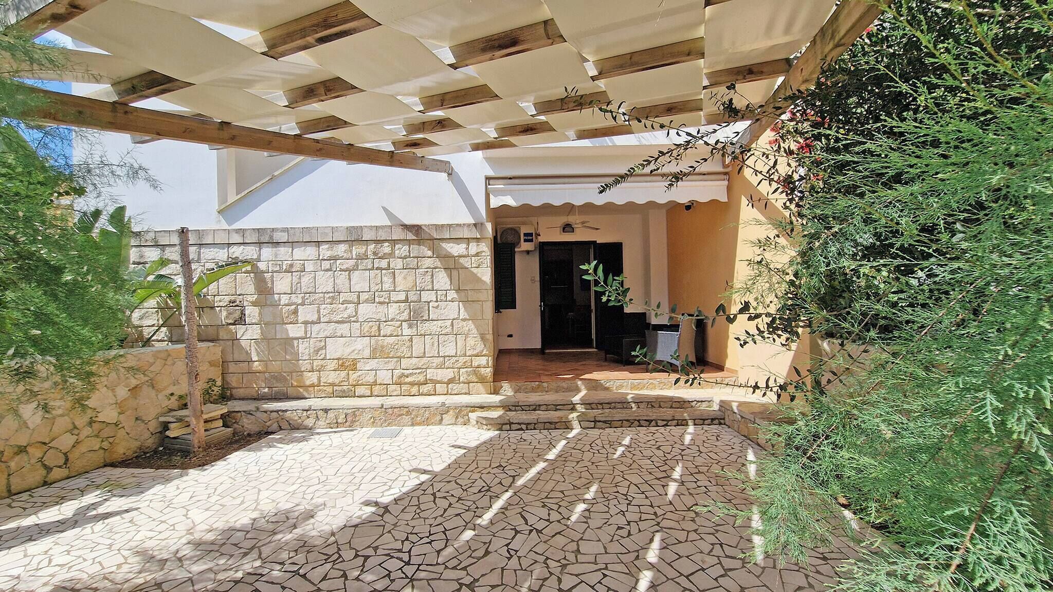 Un'area esterna coperta con pareti in pietra e pavimento piastrellato, che conduce all'ingresso di un edificio.