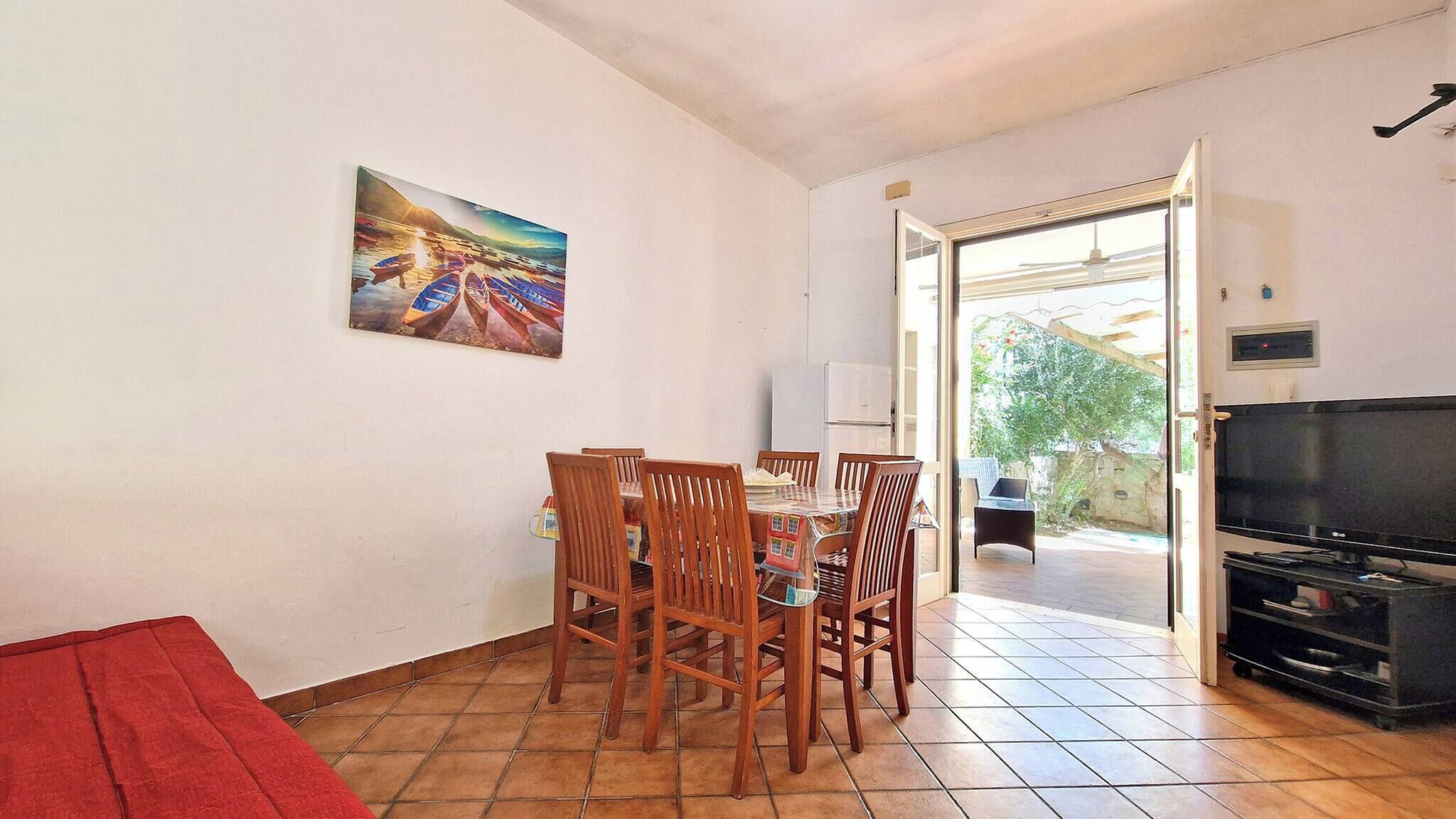 Zona pranzo con tavolo e sedie, televisione e un quadro appeso al muro.
