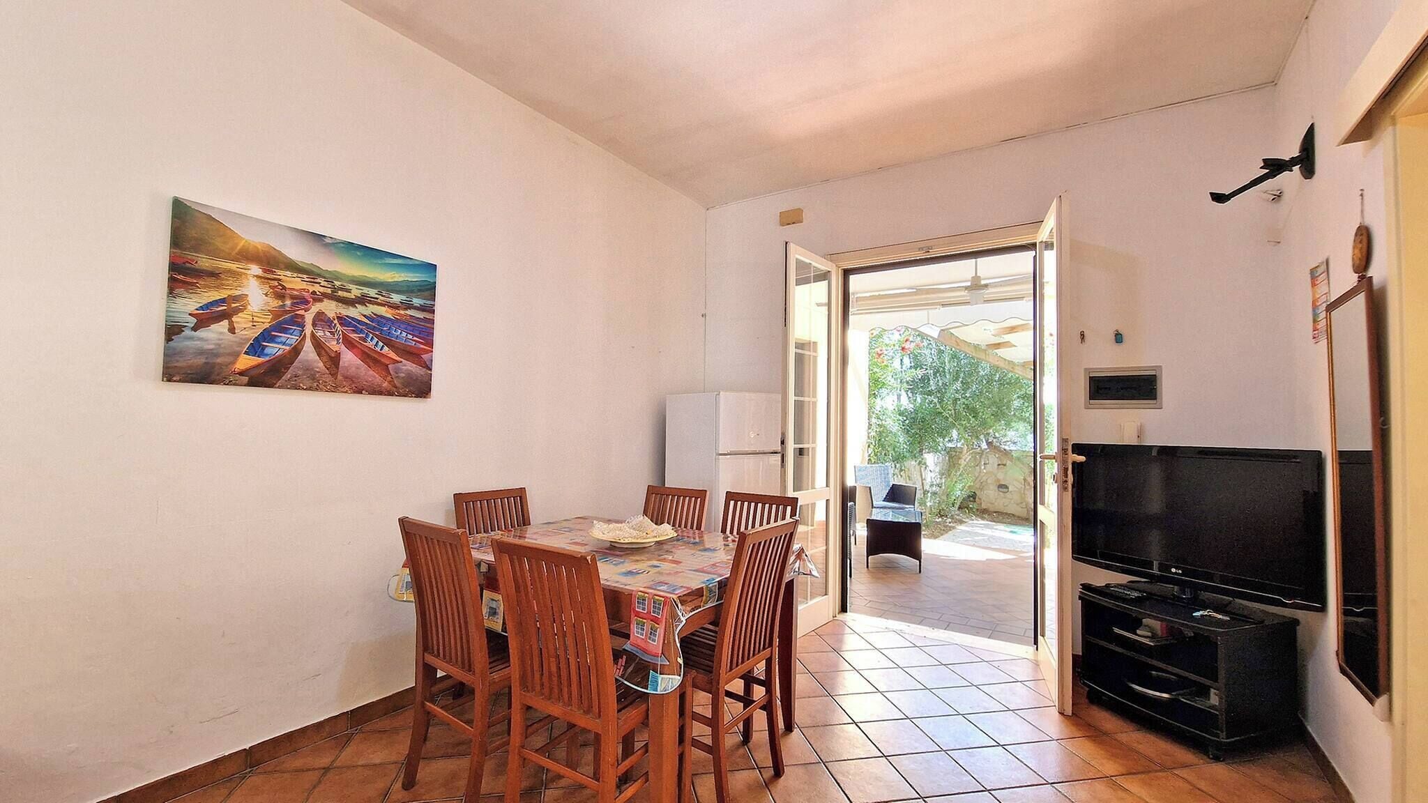 Zona pranzo con tavolo e sedie, un quadro appeso al muro, una televisione e una porta che dà su un'area esterna.