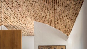 Ein Schlafzimmer mit schräg steilender Decke, einem Holzschrank, einem Bett mit dunkler Bettdecke und einer Wandleuchte.