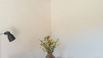 Une pièce d’angle avec un plafond en briques, des murs blancs, une table ronde en bois avec deux chaises, un vase avec des fleurs et un lampadaire noir.
