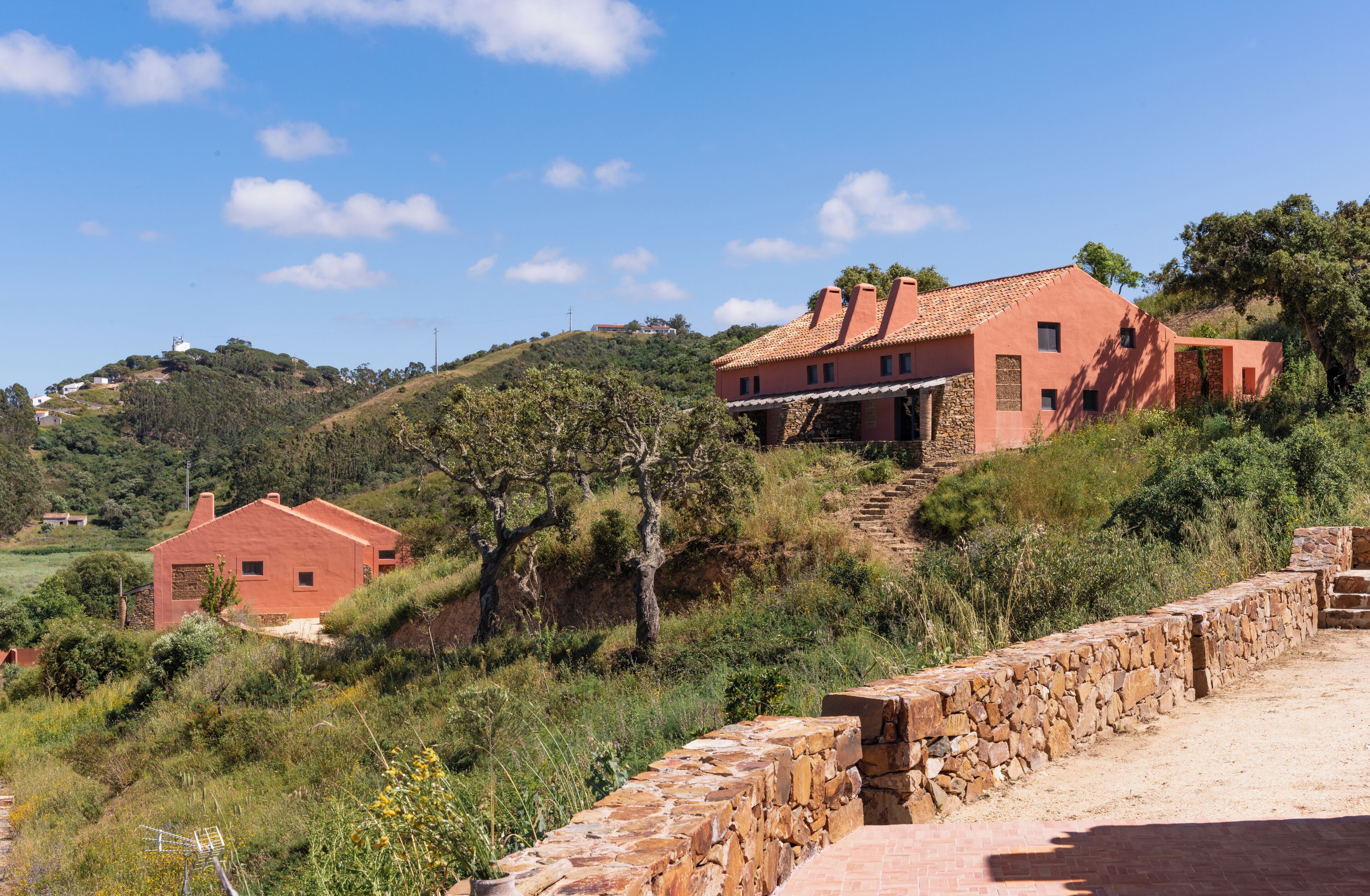 Une propriété située sur une colline, avec une maison à toit rouge, des murs en pierre et un escalier en pierre menant à la maison.