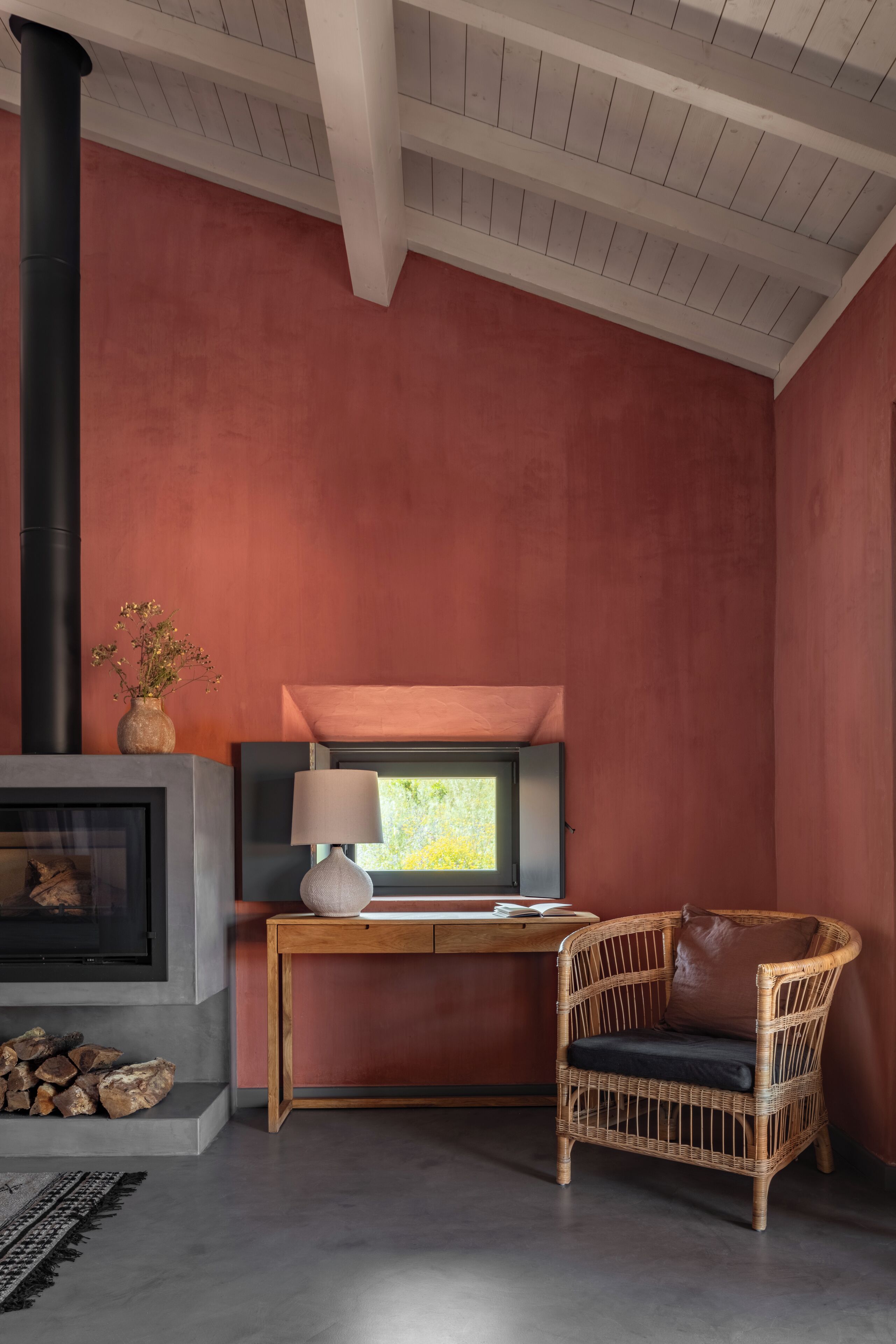 A cozy room with a fireplace, a wicker chair, and a wooden table with a lamp.