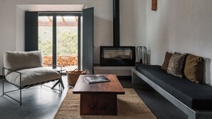 Ein modernes Wohnzimmer mit Sofa, Sessel, Couchtisch, Kamin und Blick durch eine Glastür.