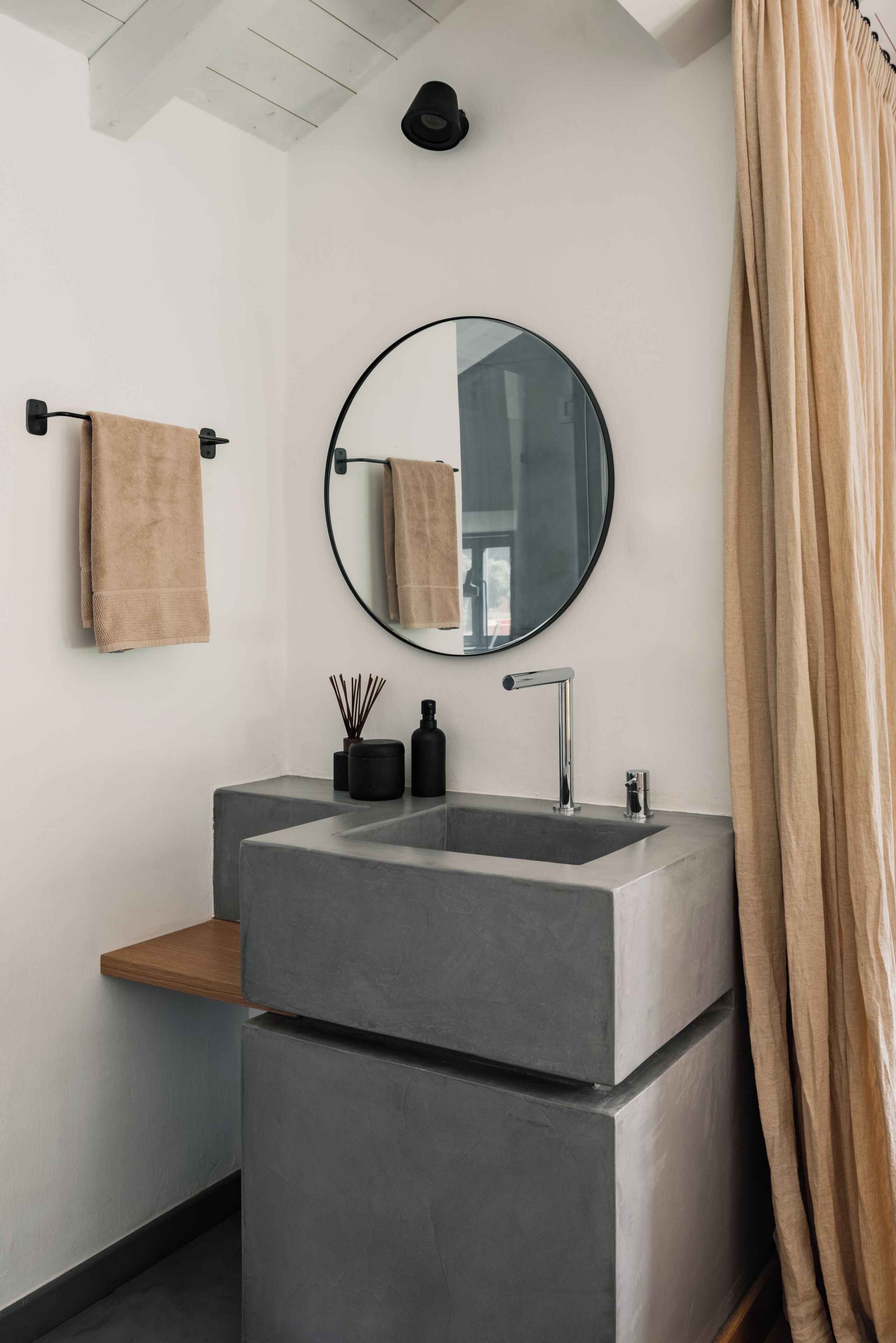 A modern bathroom with a large rectangular sink, a round mirror, and a beige towel on a towel rack.