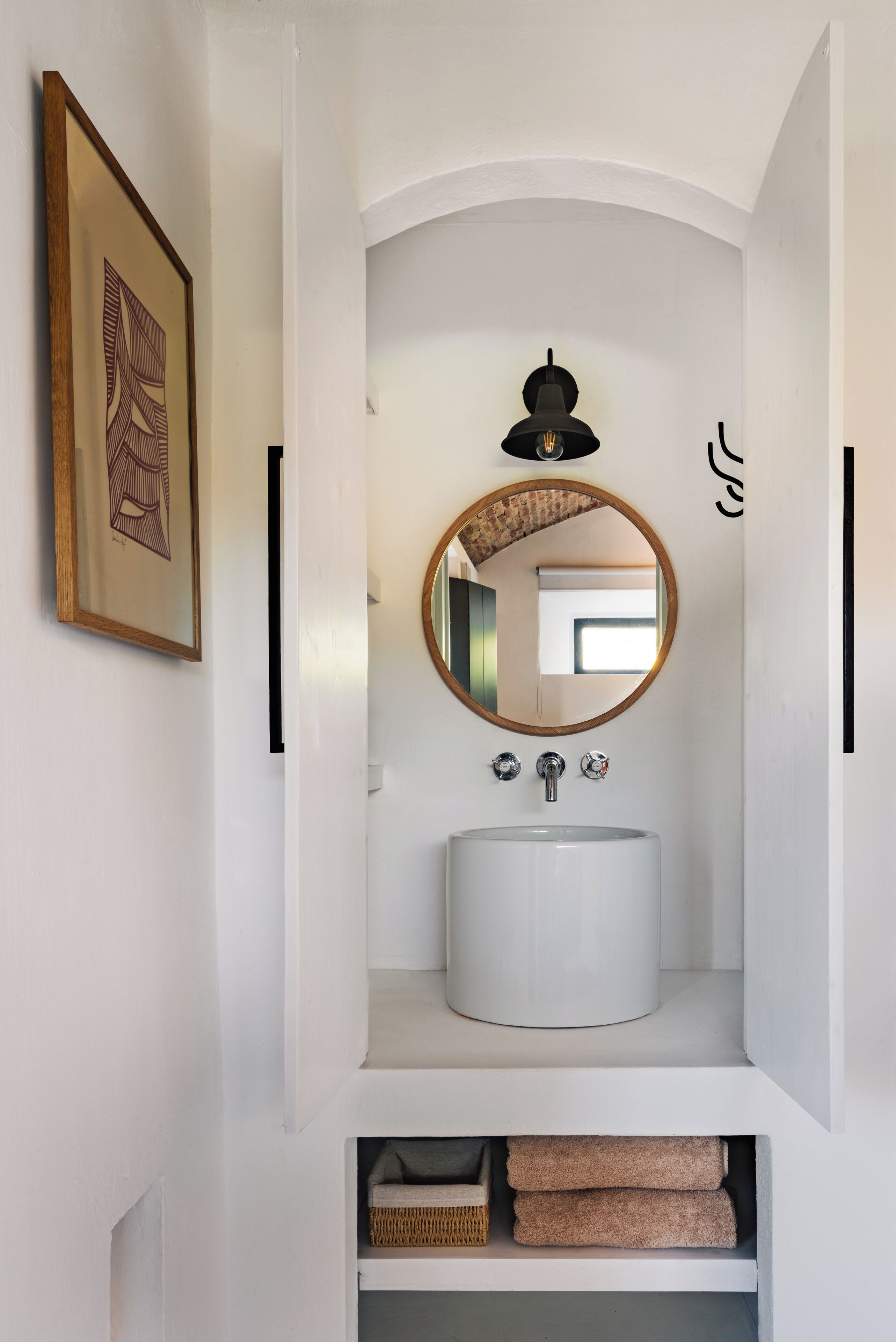 A compact bathroom with a white sink, a round mirror, and a black pendant light.