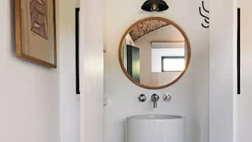 A compact bathroom with a white sink, a round mirror, and a black pendant light.