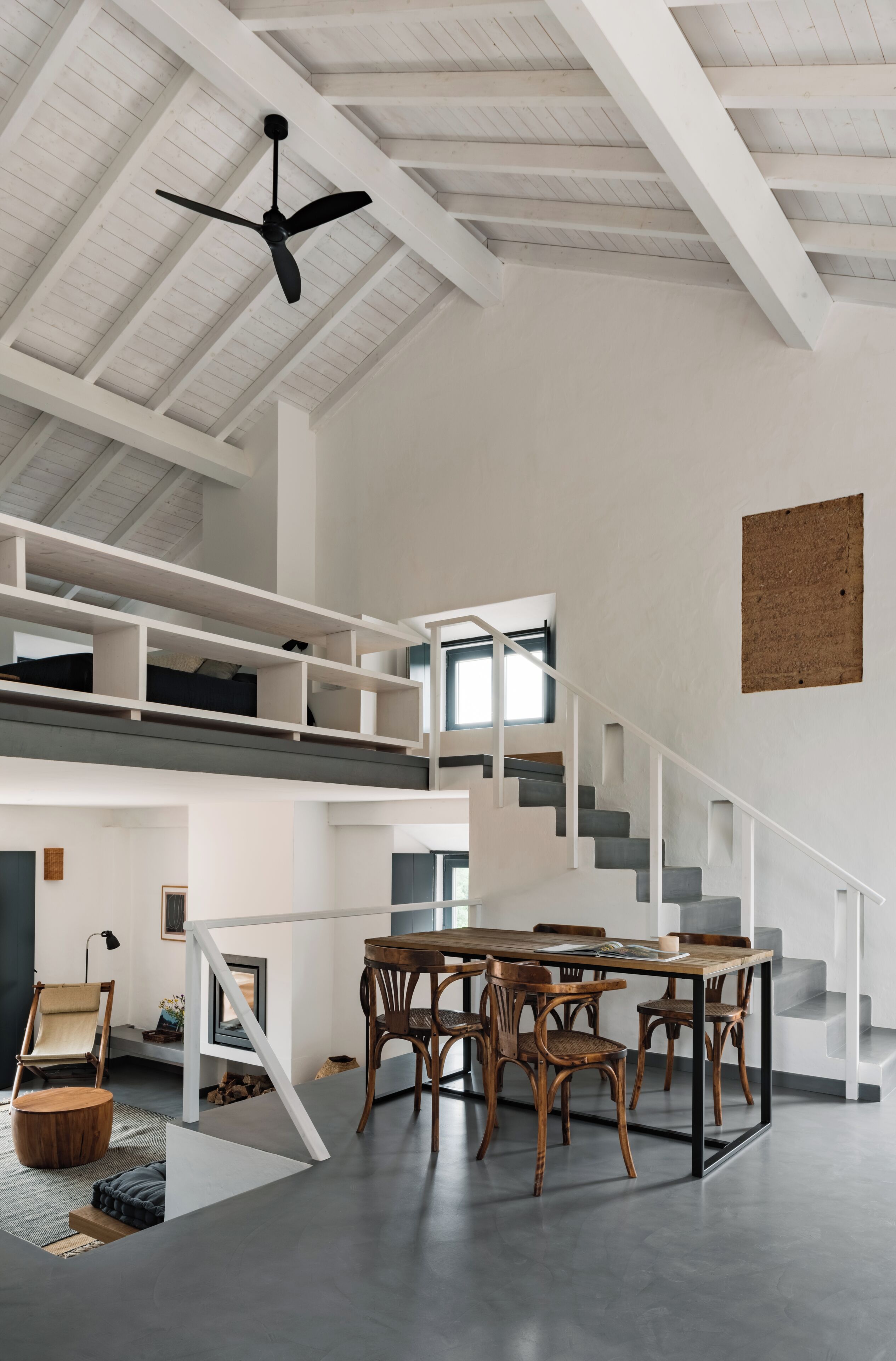 A spacious interior with a high ceiling, a central staircase, and a dining area with wooden furniture.