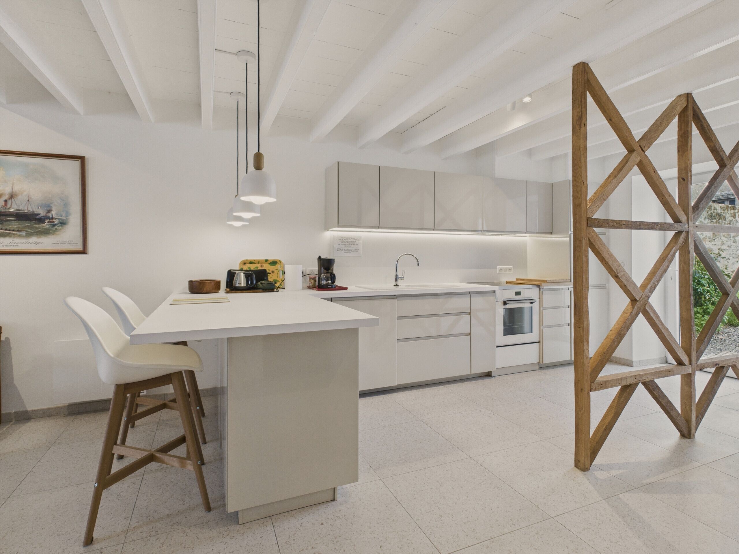 A modern kitchen with white cabinetry, a central island, and a wooden-framed window.