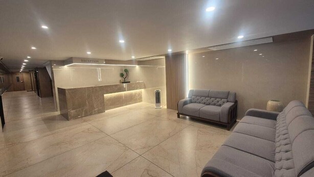 Ein moderner Empfangsbereich mit einem мраморному Receptionstresen, einem grauen Sofa und einem großen Spiegel.
