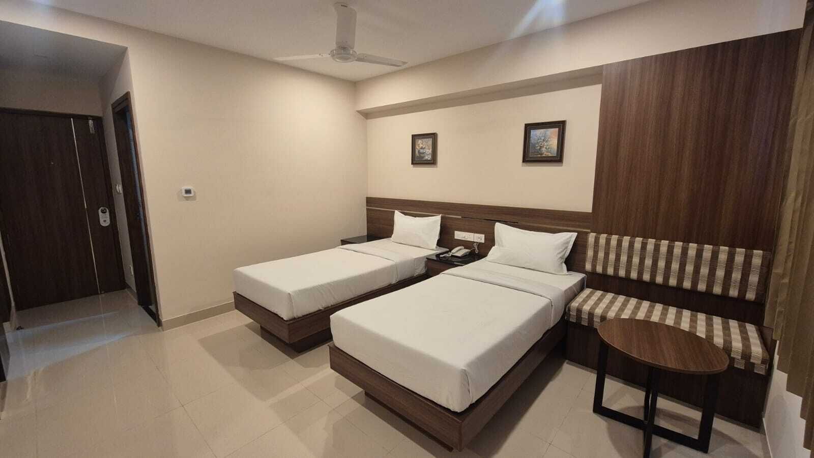 A hotel room with two single beds, a sofa, a small table, and a ceiling fan.