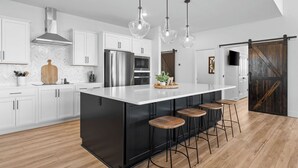 Een moderne keuken met witte kastjes, een groot kookeiland met krukken, roestvrijstalen apparatuur en een houten deur in boerderijstijl.