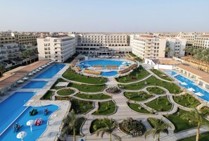 Een hotel met meerdere zwembaden, een centrale binnentuin met palmbomen en uitzicht op de omliggende stad.