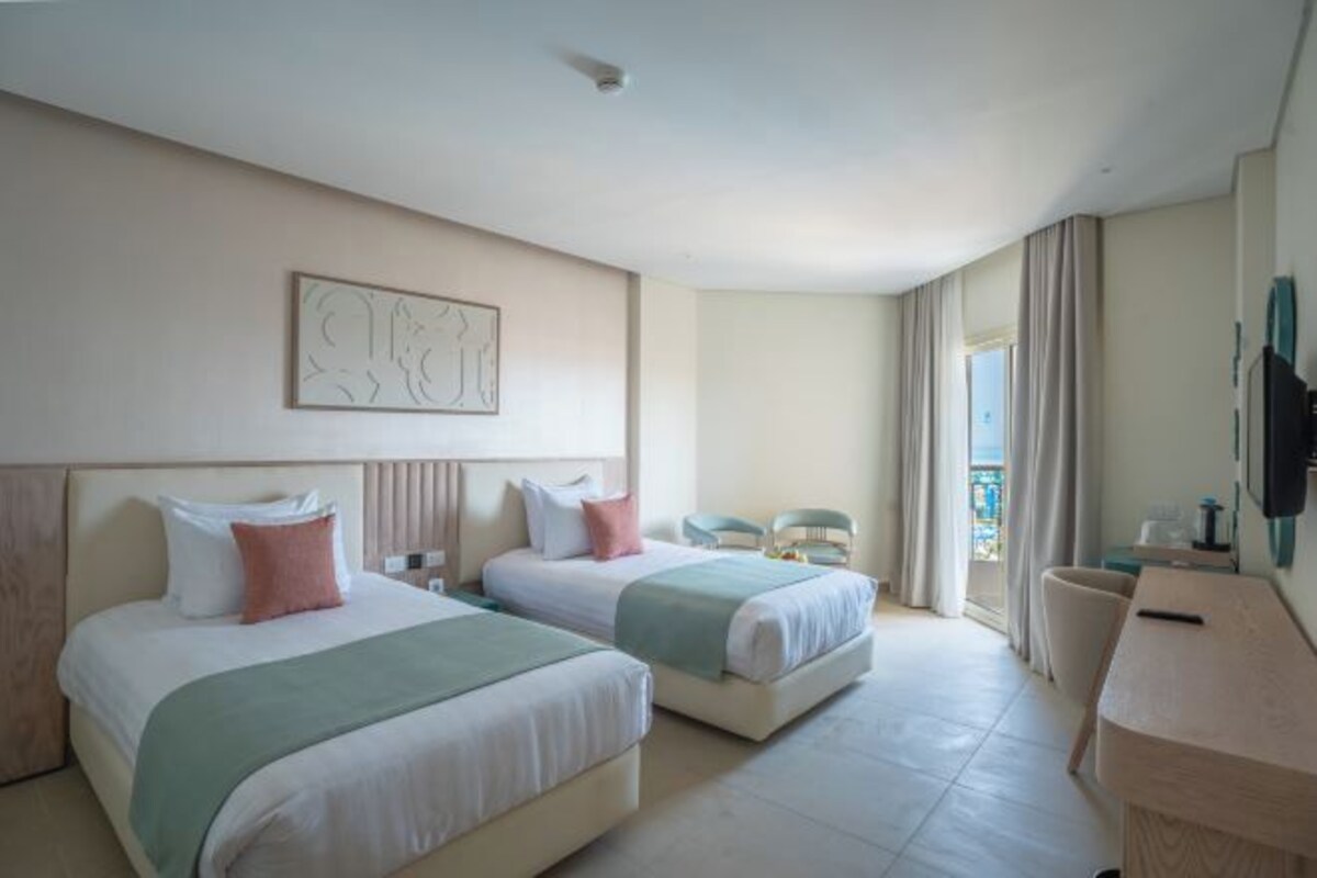 Une chambre d’hôtel avec deux lits, un bureau, une chaise et un balcon avec des rideaux.
