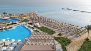 Un complexe hôtelier doté d’une grande piscine, de parasols de plage et d’une jetée qui s’avance dans la mer.