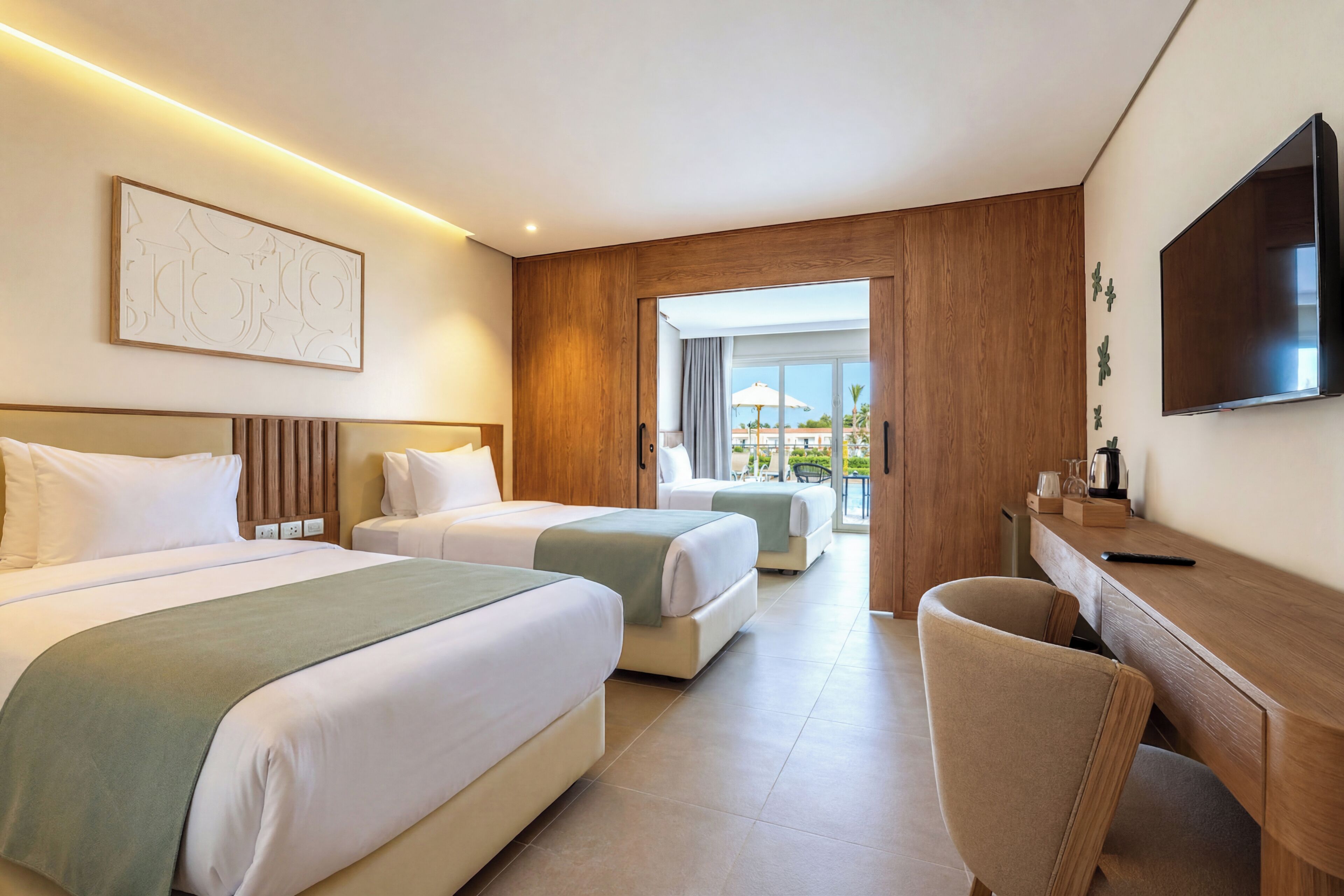 A hotel room with two beds, a desk, a chair, a flat-screen TV, and a balcony with a view.