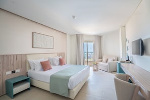 Habitación de hotel con cama, escritorio, silla, televisor y vistas al balcón.