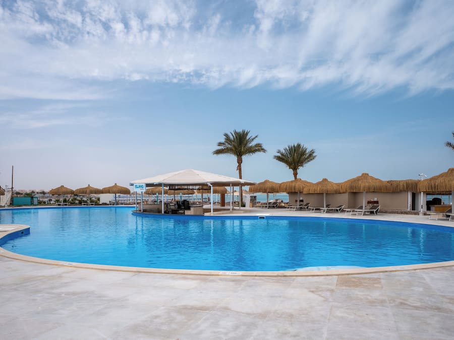 Una grande piscina con lettini e ombrelloni, circondata da palme e un cielo sereno.