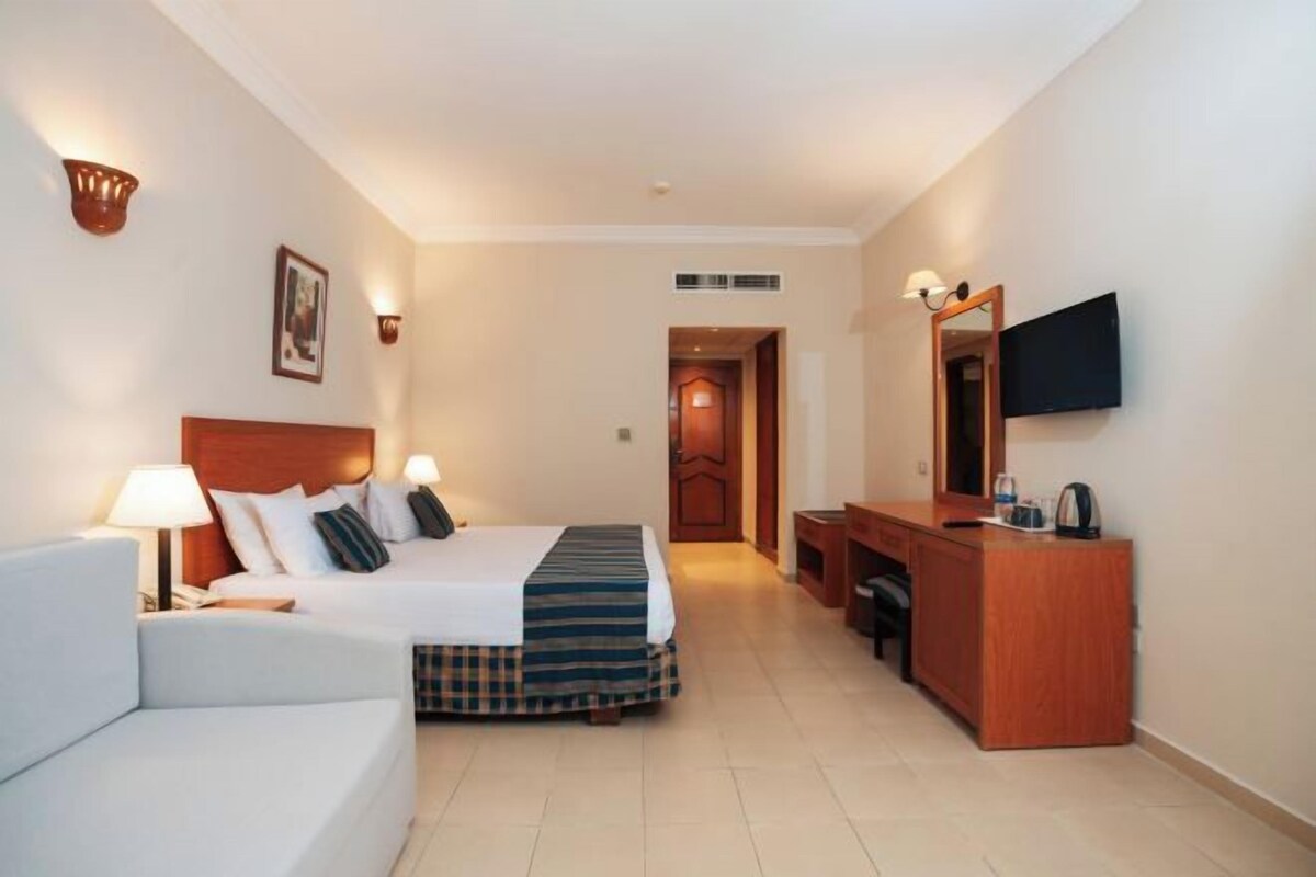Une chambre d’hôtel avec un lit, un bureau, une chaise, une télévision et une porte de salle de bain.