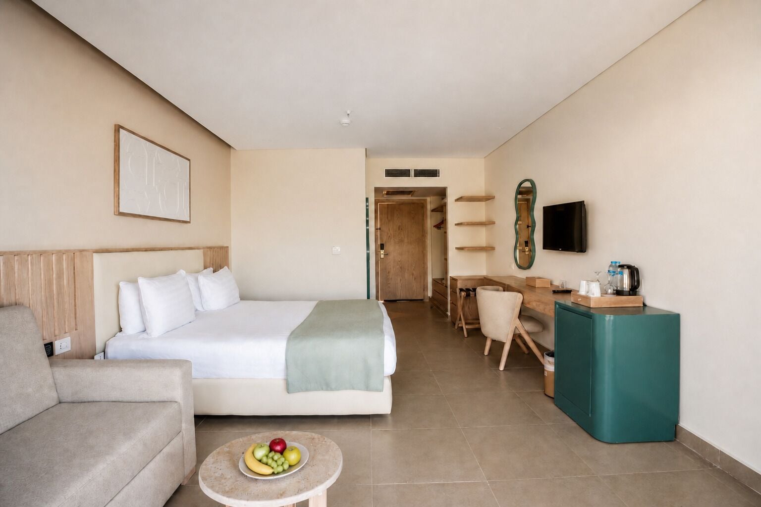 A hotel room with a bed, a desk, a television, and a small table with fruit.