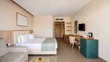 A hotel room with a bed, a desk, a television, and a small table with fruit.
