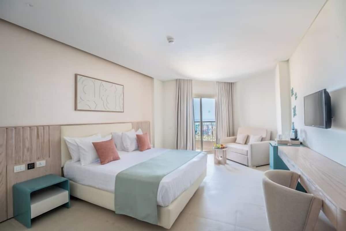 Habitación de hotel con cama, escritorio, silla, televisor y ventana con cortinas.