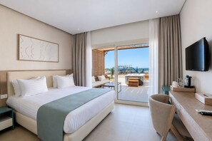 A hotel room with a bed, a desk, a TV, and a view of the beach.