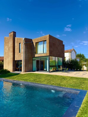 Une maison moderne à deux étages, avec une piscine en premier plan.