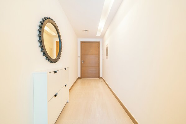 Ein schmaler Flur mit einer Holztür am Ende, einem Spiegel an der linken Wand und einem weißen Schrank.
