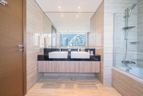 A modern bathroom with a double sink vanity, a glass shower enclosure, and a view of a cityscape through a large window.